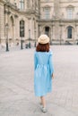 Back view of beautiful elegant young lady in hat and blue dress, walking near the vintage building in European city Royalty Free Stock Photo