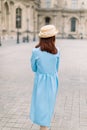 Back view of beautiful elegant young lady in hat and blue dress, walking near the vintage building in European city Royalty Free Stock Photo