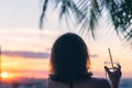 Back view of a beautiful girl with mineral water in a glass against the background of the sea in branches of palm trees. Sunset