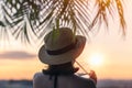 Back view of a beautiful girl with mineral water in a glass  in a straw hat against the background of the sea in branches of palm Royalty Free Stock Photo