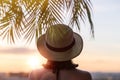 Back view of a beautiful girl in a straw hat against the background of the sea in branches of palm trees. Sunset beach. Summer Royalty Free Stock Photo