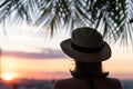 Back view of a beautiful girl in a straw hat against the background of the sea in branches of palm trees. Sunset beach. Summer Royalty Free Stock Photo