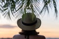 Back view of a beautiful girl in a straw hat against the background of the sea in branches of palm trees. Sunset beach. Summer Royalty Free Stock Photo