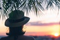 Back view of a beautiful girl in a straw hat against the background of the sea in branches of palm trees. Sunset beach. Summer Royalty Free Stock Photo