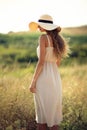 Back view of beautiful girl who walks on field while wearing a sunhat and midi dress. Lifestyle