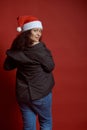 Back view beautiful ethnic young adult pregnant woman wearing Santa hat, smiles cutely looking at camera, red background