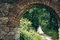 Back view of the beautiful walking newlywed couple by the hand along the path of the green forest. Look through the old