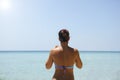 Back view of beautiful woman standing in front of the sea. Perhaps she watching your smartphone. Summer vibes. Beautiful sky and