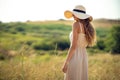 Back view of beautiful woman who walks on field while wearing a sunhat and midi dress. Lifestyle