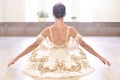 Back view of beautiful ballerina in cream dress sitting and warms up her hands on wooden floor in ballet studio Royalty Free Stock Photo