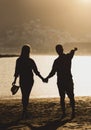 Back view of a beautiful young couple of teenagers holding their hands standing on the beach during sunset Royalty Free Stock Photo