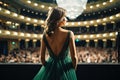 back view of beautiful young woman in green dress standing in auditorium, Back view of a girl in a green evening dress on the