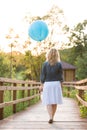 Back view on beautiful young woman standing on wooden bridge and holding big blue balloon on the sunset in the park Royalty Free Stock Photo