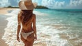 Back view of a beautiful young woman in white bikini and straw hat standing on the beach and looking at the sea Royalty Free Stock Photo