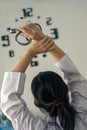 Behind young female doctor holding stethoscope standing and hand up for relaxing after finish work with clock on the wall. Royalty Free Stock Photo