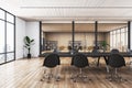 Back view on black meeting table surrounded by dark wheel chairs on wooden floor in stylish conference room with glass wall