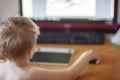 Back view of blond caucasian baby boy with computer mouse and graphics tablet, looking to the screen.