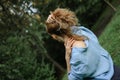 Back view of blonde adult woman wearing blue casual jeans blouse posing in the park on green trees background. Hipster Royalty Free Stock Photo