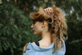 Back view of blonde adult woman wearing blue casual jeans blouse posing in the park on green trees background. Hipster Royalty Free Stock Photo