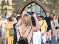 Back view of a blonde unrecognizable woman tourist on Charles Bridge, Prague, taking pictures with her smartphone