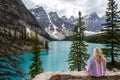 Back view of a blonde woman cuddled in a pink blanket, looking at Moranie Lake in Canada