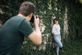 Back view of blurred man taking photos of woman who is posing near wall