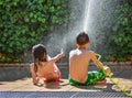 back view of a boy and a girl wearing swimsuit having a fun time of summer in a terrace of a garden playing with a hose refreshing