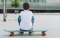 Back view. Boy in white T-shirt and blue jeans, sits on city street on skateboard. Space for text, logo, image. Mock up.