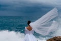 Back view of brunette bride in white wedding dress and bridal veil on a cloudy day. Romantic beautiful bride posing near the sea Royalty Free Stock Photo