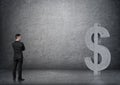 Back view of a businessman looking at big 3D concrete dollar sign.