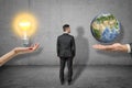 Back view of businessman standing between two big hands, woman`s hand levitating lightbulb, man`s hand levitating little