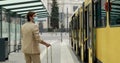 Back view of businessman in stylish formal suit with white suitcase entering yellow tram on stop.