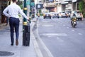 Back view of businessman walking pulling suitcase on the sidewalk. Traffic jams in the city. Lifestyle traveler young man holding