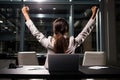 Back view of businesswoman sitting at desk and raising arms in office, Excited girl sitting at her desk with a laptop and