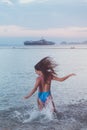 Back view of carefree young woman with her hair streamed running into sea splashing water at sunset a ship on horizon. Royalty Free Stock Photo