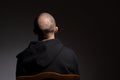 Back view of casual bald young man in black hoodie on dark background with copyspace