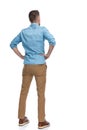 Back view of casual young man holding hands on hips and looking away