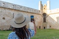 Back view of Caucasian woman taking photo of medieval castle through phone