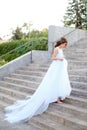 Back view of caucasian young bride walking on concrete stairs and wearing white dress. Royalty Free Stock Photo