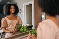 Back view of cheerful African young woman holding contour palette and brush, looking at mirror and smiling in home Royalty Free Stock Photo