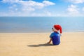 back view of child boy in santa hat, sunglasses and swimsuit sitting on the sand beach Royalty Free Stock Photo