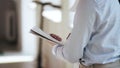 Back view close-up, businessman in white formal shirt holding paper notepad, writing in modern light office workplace.