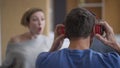 Back view close-up man putting on headphones ignoring woman yelling at background gesturing. Tired Caucasian husband