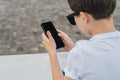 Back view. Close-up of smartphone in hands of boy. Teenager sits outdoor,uses gadget, browsing internet, checking email. Royalty Free Stock Photo