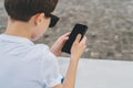 Back view. Close-up of smartphone in hands of boy. Teenager sits outdoor,uses gadget, browsing internet, checking email. Royalty Free Stock Photo