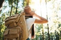 Back view of close-up traveler backpack and hipster girl wearing hat. Young brave woman traveling alone among trees in forest on o