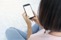 Back view close up of a woman hand holding and using smart phone with white blank empty screen sitting on a bed at home Royalty Free Stock Photo