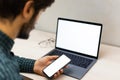 Back view close-up of young guy holding modern smartphone with mockup beside laptop on work desk. Royalty Free Stock Photo