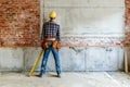 Back view of a construction worker with tools standing in front of a brick wall, wearing a yellow helmet. Industrial Royalty Free Stock Photo