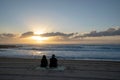Back view of a couple sitting on the sandy beach watching the sea during cloudy sunset Royalty Free Stock Photo